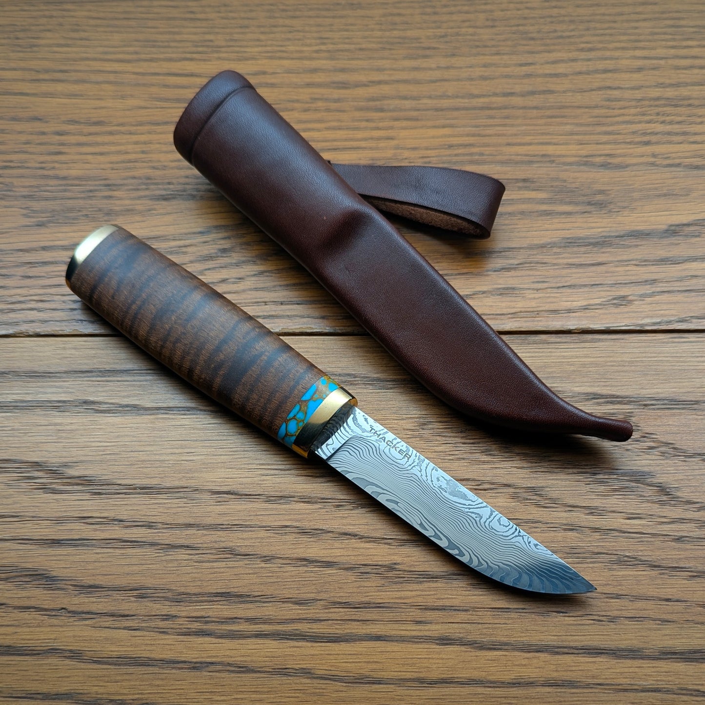 Knife with damascus blade and wooden handle on a wooden surface with leather sheath